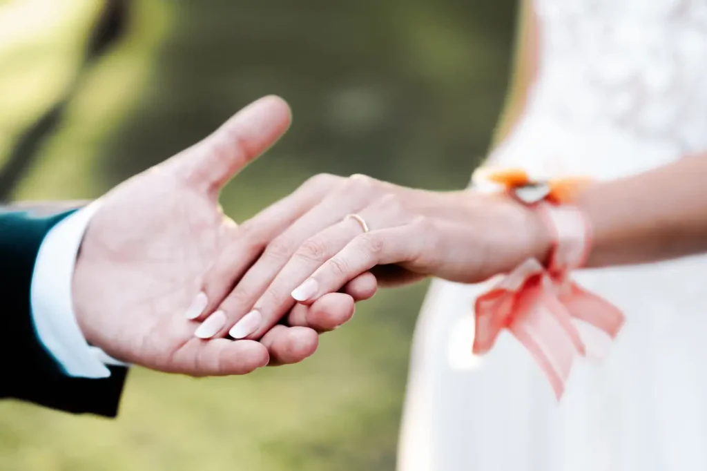 Détail des mains enlacées des mariés et alliance de la mariée