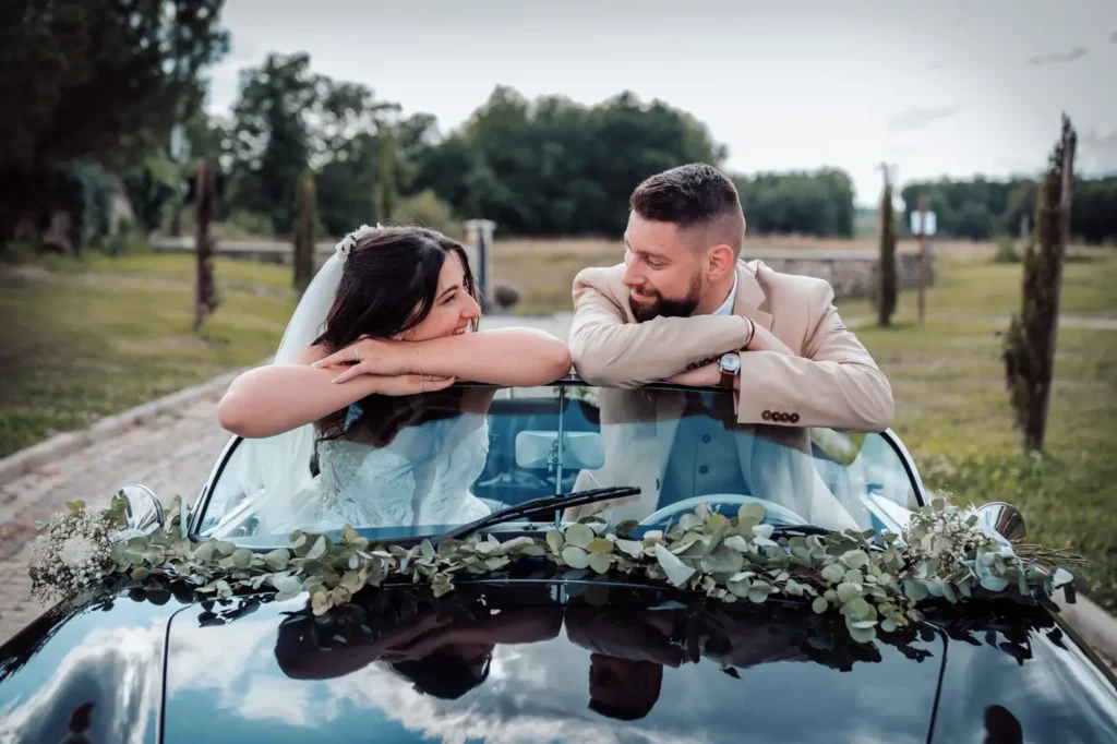 Mariés appuyés sur une voiture ancienne