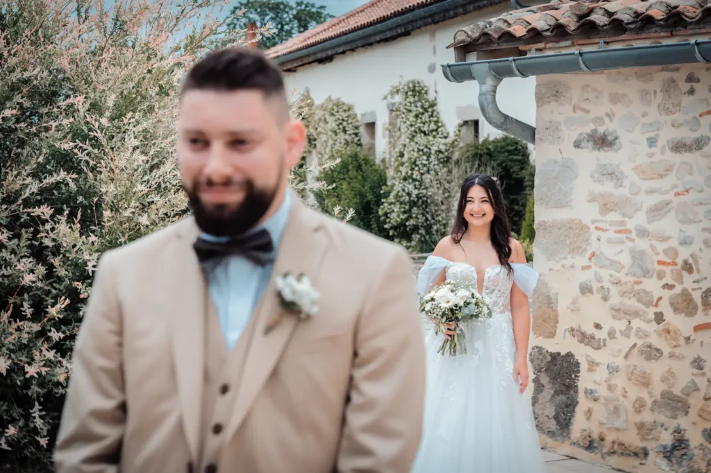 Portrait du marié avec la mariée en fond qui le regarde de dos