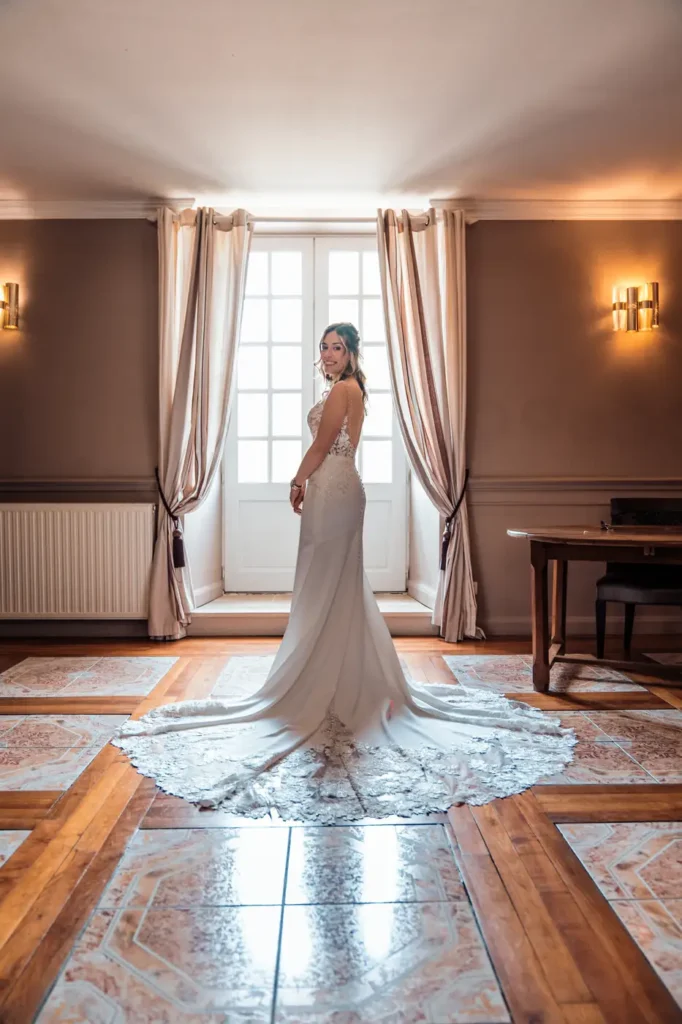 Mariée en robe élégante près d’une fenêtre au château